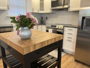 Una cocina con armarios blancos, horno de acero inoxidable y una mesa de madera con un florero.