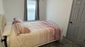 Un dormitorio con cama, mesita de noche, ventana con cortinas y puerta.