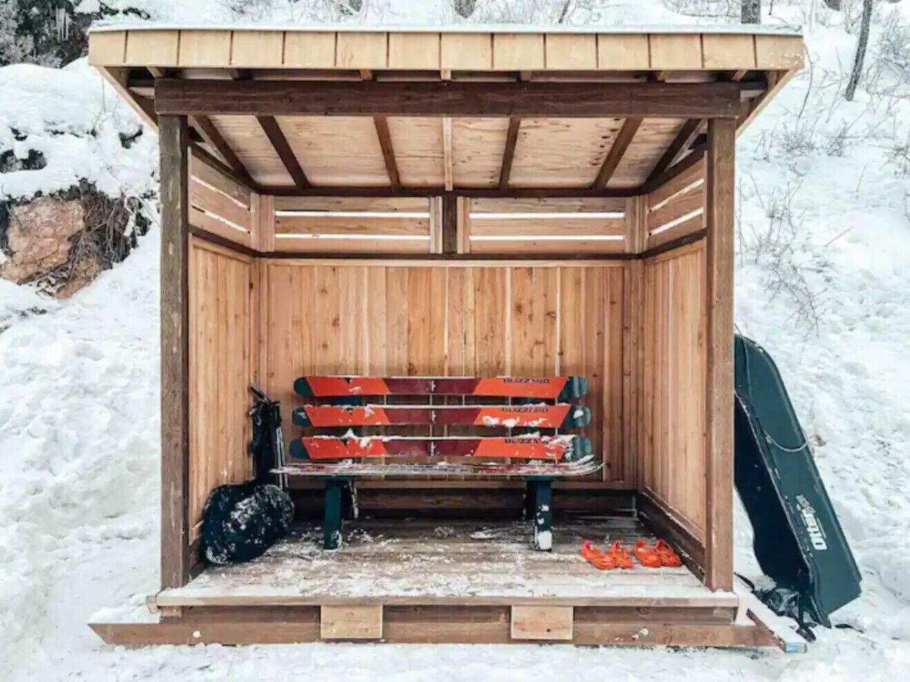 A wooden sauna structure with benches and a bench seat, surrounded by snow.