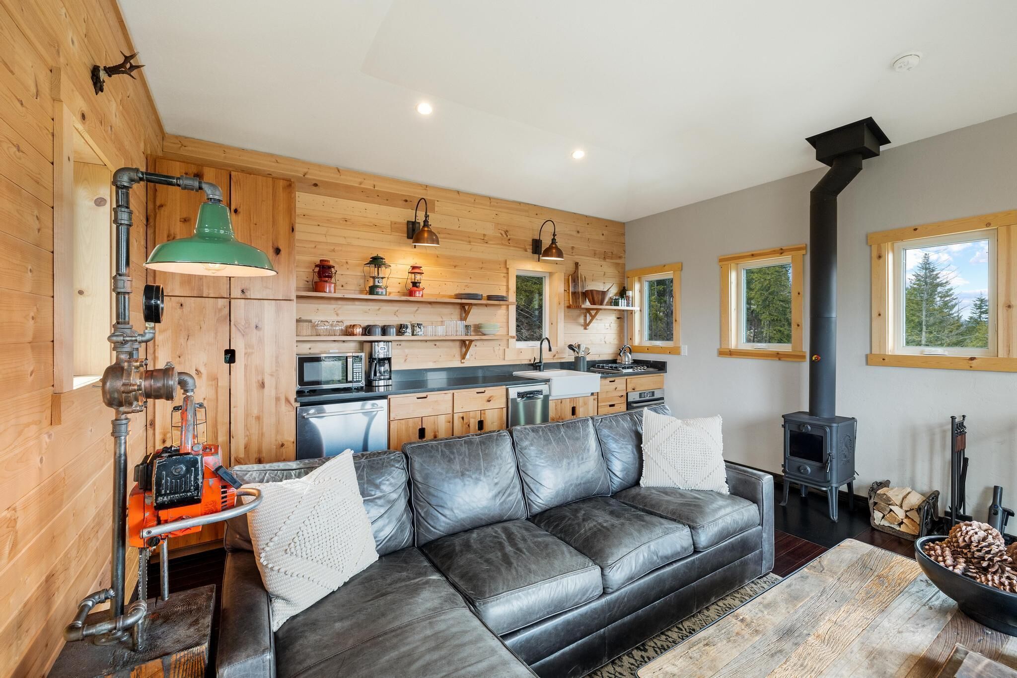 A cozy cabin interior with a leather sofa, wooden walls, a kitchen with a stove, and a fireplace.