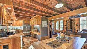A rustic kitchen with wooden cabinets, a stainless steel refrigerator, and a dining area with a wooden table and chairs. - Unadilla Cabin on 50 Acres + Fire Pit & Creek (Unadilla)
