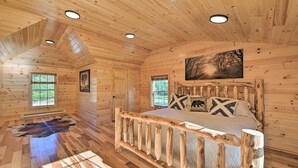 A log cabin bedroom with a bed, windows, and a painting on the wall. - Unadilla Cabin on 50 Acres + Fire Pit & Creek (Unadilla)
