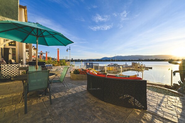 Una terrazza esterna con vista sull'acqua, sedie, un tavolo e un ombrellone grande.