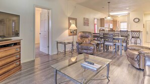 A living room with a glass coffee table, leather armchairs, a TV, and a dining area with a chandelier. - Cozy Condo w/ Nature Views: Branson Getaway (Branson West)