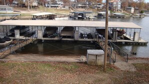 A docked boat house with covered seating areas and a small dock extending into the water. - Charming Lake View Cabin Retreat Near Captain Ron's Resort, Lake of the Ozarks (Sunrise Beach)