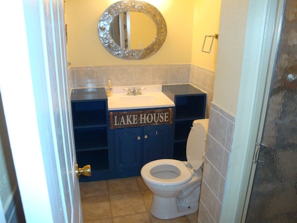 A bathroom with a toilet, a sink, and a mirror. There is a sign that reads "LAKE HOUSE" above the sink. - Charming Lake View Cabin Retreat Near Captain Ron's Resort, Lake of the Ozarks (Sunrise Beach)