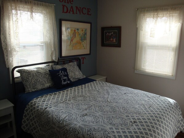 Ein Schlafzimmer mit einem Bett, zwei Kissen, einem Nachttisch und einer Wand mit einem gerahmten Bild und einem Schild mit der Aufschrift 'ONE DANCE'.