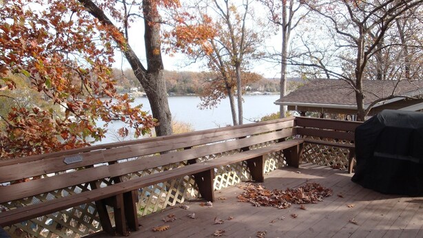 A wooden deck with a bench and a grill, overlooking a lake with trees in autumn colors. - Charming Lake View Cabin Retreat Near Captain Ron's Resort, Lake of the Ozarks (Sunrise Beach)