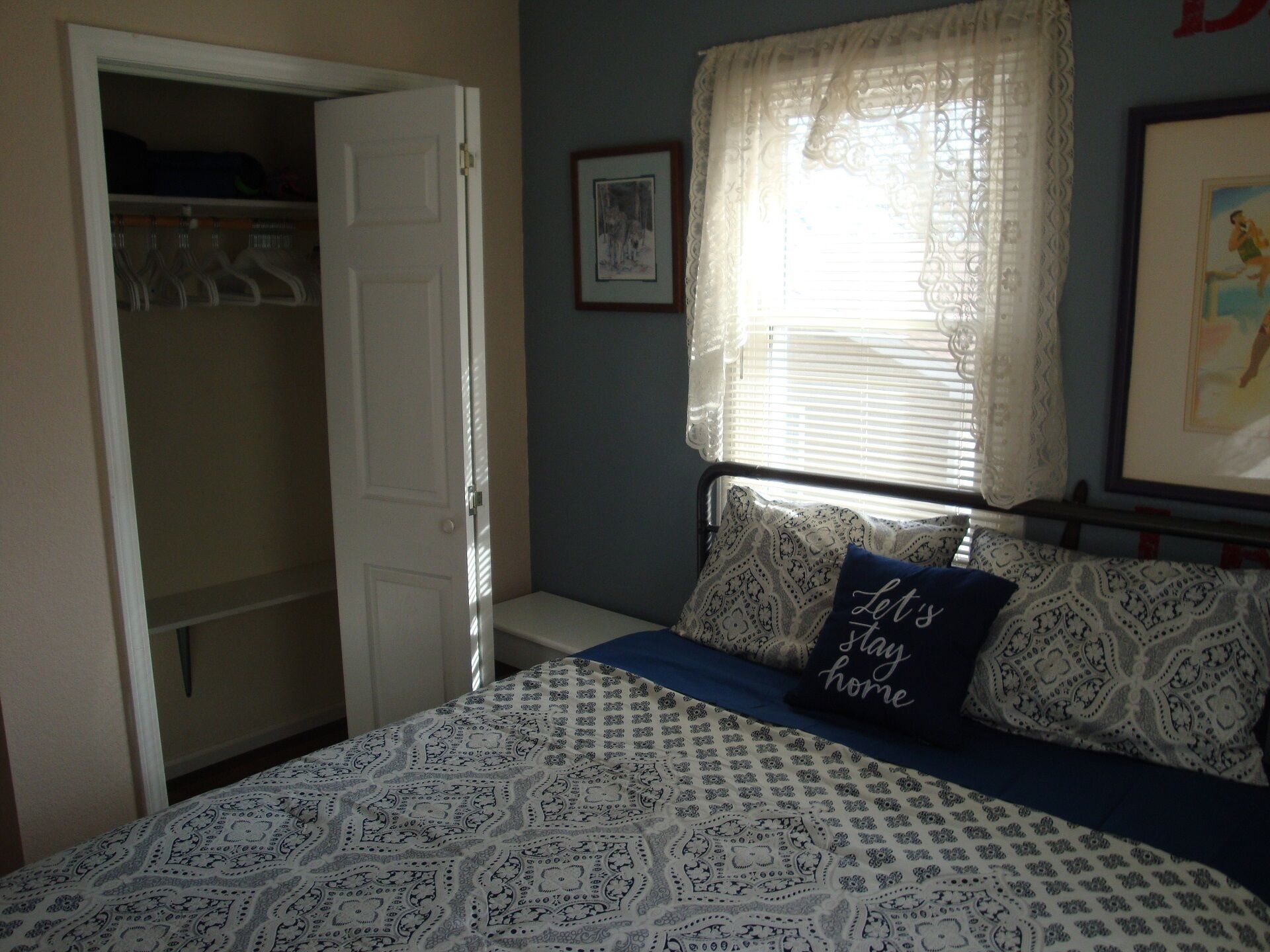 A bedroom with a bed, a wardrobe, a window with curtains, and a framed picture on the wall.