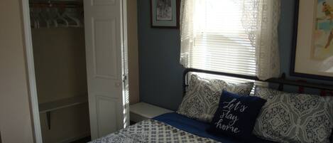 A bedroom with a bed, a wardrobe, a window with curtains, and a framed picture on the wall.