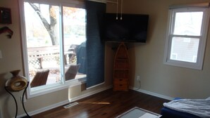 A room with hardwood flooring, a television mounted on the wall, a window with a view of the outdoors, and a small wooden cabinet. - Charming Lake View Cabin Retreat Near Captain Ron's Resort, Lake of the Ozarks (Sunrise Beach)