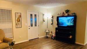 A living room with a wooden floor, a television on a stand, a door with frosted glass panels, and a small table with a plant. - Country Living in Oxford (Oxford)
