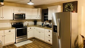 A kitchen with white cabinets, stainless steel appliances, a granite countertop, and a wooden floor. - Country Living in Oxford (Oxford)