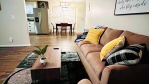 A living room with a brown sofa, a coffee table with a plant, and a dining area in the background. - Country Living in Oxford (Oxford)