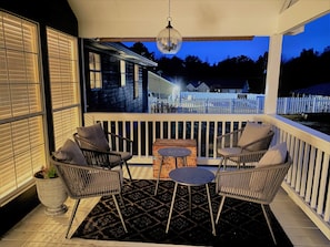 A covered porch with wicker chairs, a small table, and a hanging light fixture.