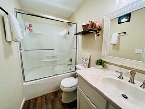 Une salle de bain avec une douche à parois de verre, des toilettes, un lavabo avec un miroir et une étagère contenant des articles de toilette.