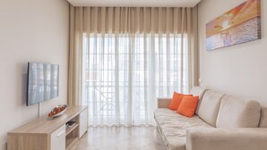 Ein modernes Wohnzimmer mit einer Couch, einem Fernseher und einem großen Fenster mit Vorhängen.