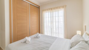 Ein Hotelzimmer mit einem großen Bett, einem Kleiderschrank, einem Fenster mit Vorhängen und einer Nachttischlampe.
