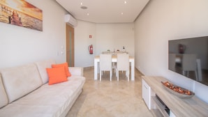 Ein modernes Wohnzimmer mit einer Couch, einem Esstisch mit Stühlen, einem Flachbildfernseher und einem Gemälde an der Wand.