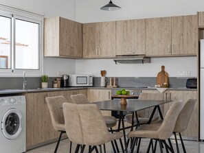 Una cocina moderna con armarios de madera, lavadora integrada, una mesa de comedor con sillas y un ventanal grande.