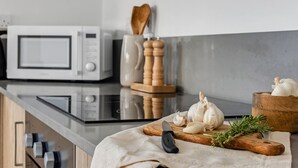 A kitchen with a microwave, wooden cutting board, garlic, a knife, and a wooden bowl. - Sanders White Mountains - Vibrant Villa With Pool (Tremithousa)