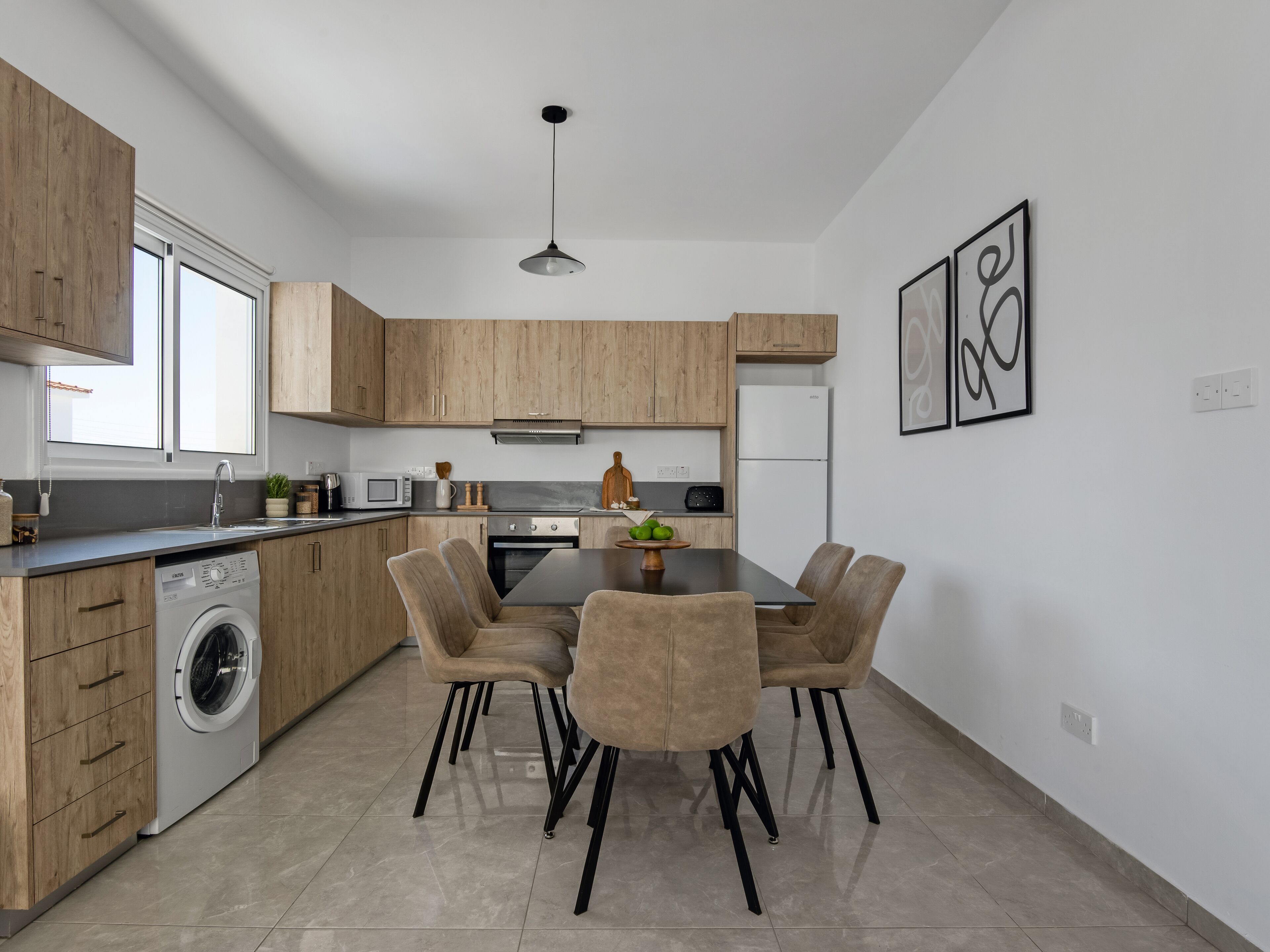 Une cuisine moderne avec des meubles en bois, un lave-linge encastré, un coin repas avec une table et des chaises, et un réfrigérateur.