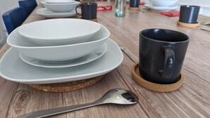 Un tavolo da pranzo con piatti impilati, una tazza nera su un sottobicchiere e un cucchiaio.