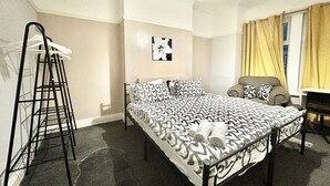 Una camera da letto con un letto, una sedia, una scrivania, una scala e un'opera d'arte appesa al muro.
