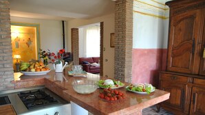 A kitchen with a gas stove, a marble countertop, and a brick wall. There is a dining area with a couch and a table set with food. - Meridiana Holiday House With Shared Swimming Pool (Itri)