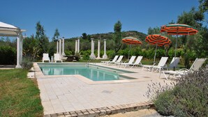 A pool area with white lounge chairs and orange striped umbrellas, surrounded by greenery and white columns. - Meridiana Holiday House With Shared Swimming Pool (Itri)