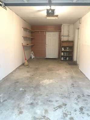 Garage features a clean space with a broom and storage shelf.