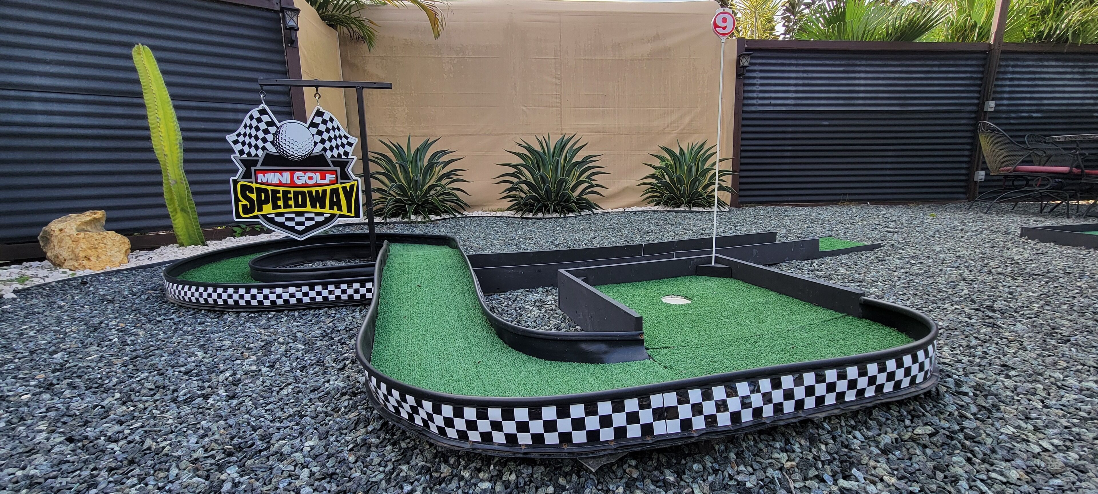 Un parcours de mini-golf avec une bordure à carreaux, une balle de golf et un panneau indiquant « Mini Golf Speedway ».