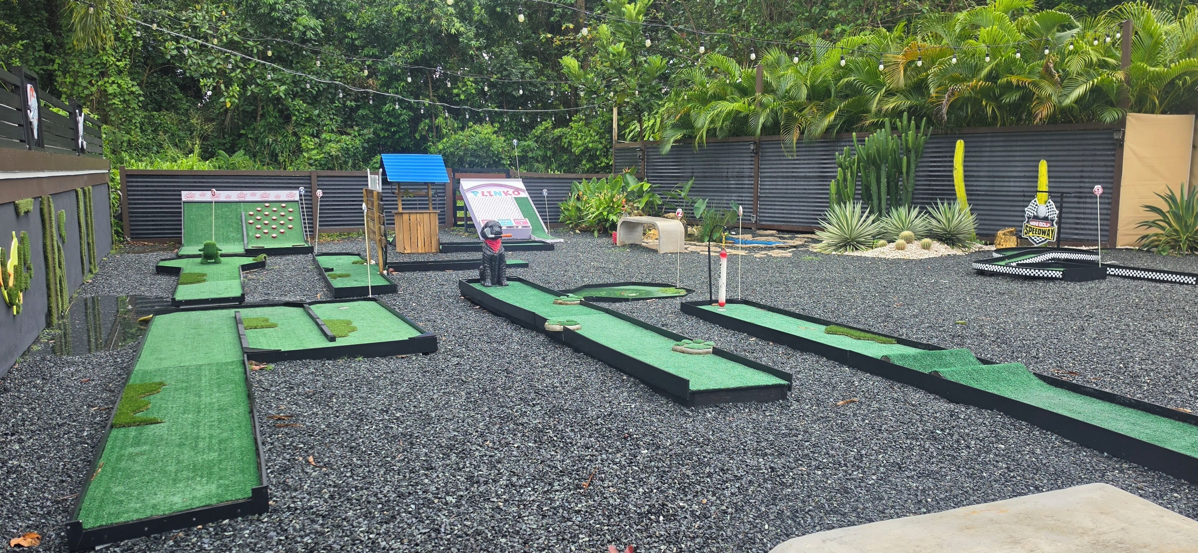 Een minigolfbaan met meerdere groene puttingmatten, een houten constructie en een bord.