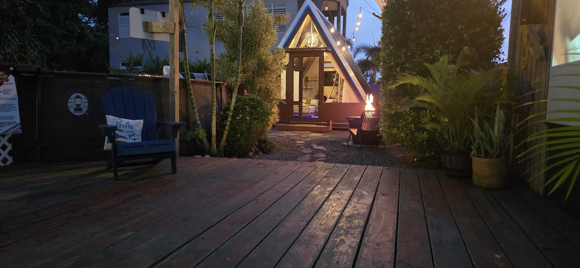 En träveranda som leder fram till en byggnad med ett triangulärt tak och en upplyst interiör.