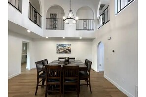 A spacious dining area with a high ceiling, wooden flooring, and a chandelier.