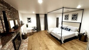Une chambre à coucher avec un lit à baldaquin, une cheminée en briques, une petite table ronde et une chaise.