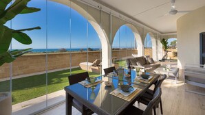 Ein großzügiger Balkon mit Glaswand und Meerblick, ausgestattet mit Esstisch, Stühlen und einer Couch.