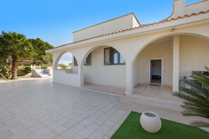 Uma villa moderna com um pátio amplo, uma área externa coberta e um vaso branco grande.
