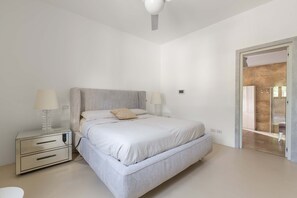 Quarto moderno com uma cama grande, mesas de cabeceira e uma porta que dá para um banheiro.