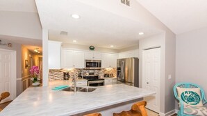 A modern kitchen with white cabinets, stainless steel appliances, and a marble island with bar stools.