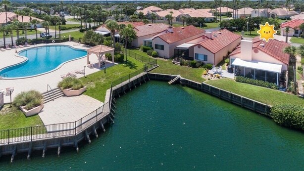 A residential area with a swimming pool, houses with red roofs, and a clear sky.