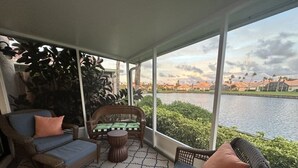 A covered patio with wicker furniture, a view of a lake, and a distant mountain.
