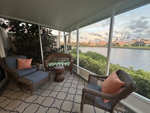A covered patio with wicker furniture, a view of a lake, and a distant mountain.