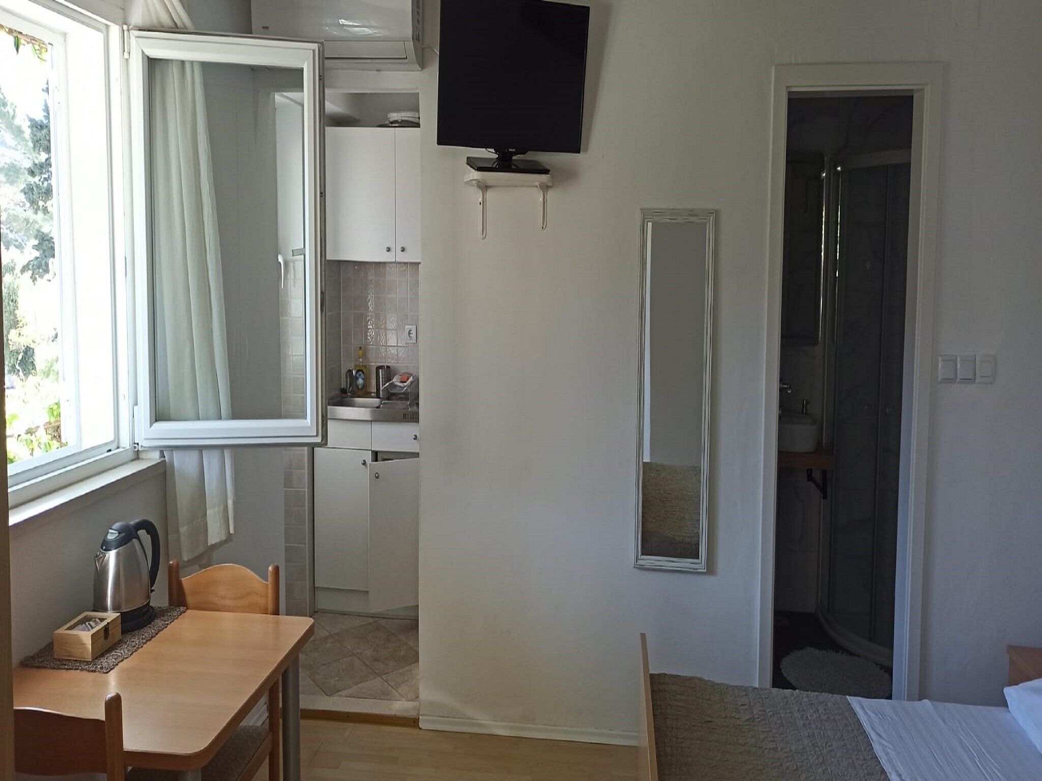 Une pièce de taille modeste comprenant un lit, une petite table, une chaise, un coin cuisine, une salle de bain et un téléviseur fixé au mur.
