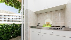 A modern kitchen with a built-in stove, a sink, and a window overlooking a stone wall and greenery. - Apartments & Rooms Jokovic (Zupa dubrovacka)