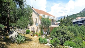 A two-story house with a tiled roof, surrounded by lush greenery and a rocky landscape. - Apartments & Rooms Jokovic (Zupa dubrovacka)