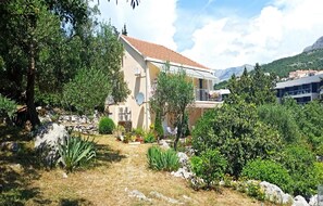 Ein zweistöckiges Haus mit einem Ziegeldach, umgeben von üppiger Vegetation und einer felsigen Landschaft.