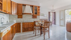 A kitchen with wooden cabinets, a tiled backsplash, and a dining area with two chairs. - 2811 Villetta Altomare by Barbarhouse (Porto Cesareo)