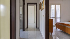A hallway leading to a bedroom with a bed, a dresser, and a window with curtains. - 2811 Villetta Altomare by Barbarhouse (Porto Cesareo)