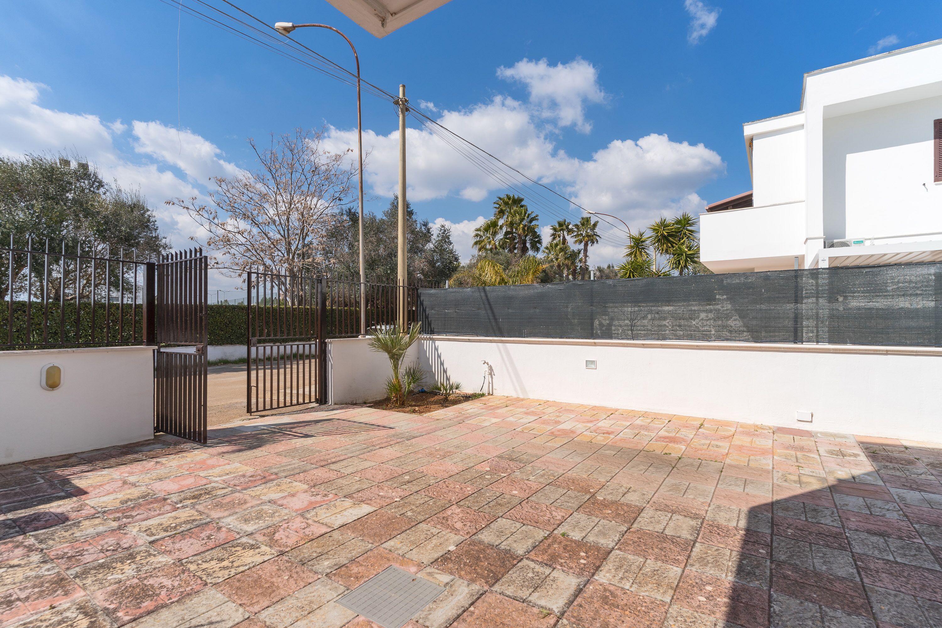 A rooftop patio with a tiled floor, a metal gate, and a white building with a black wall in the background.